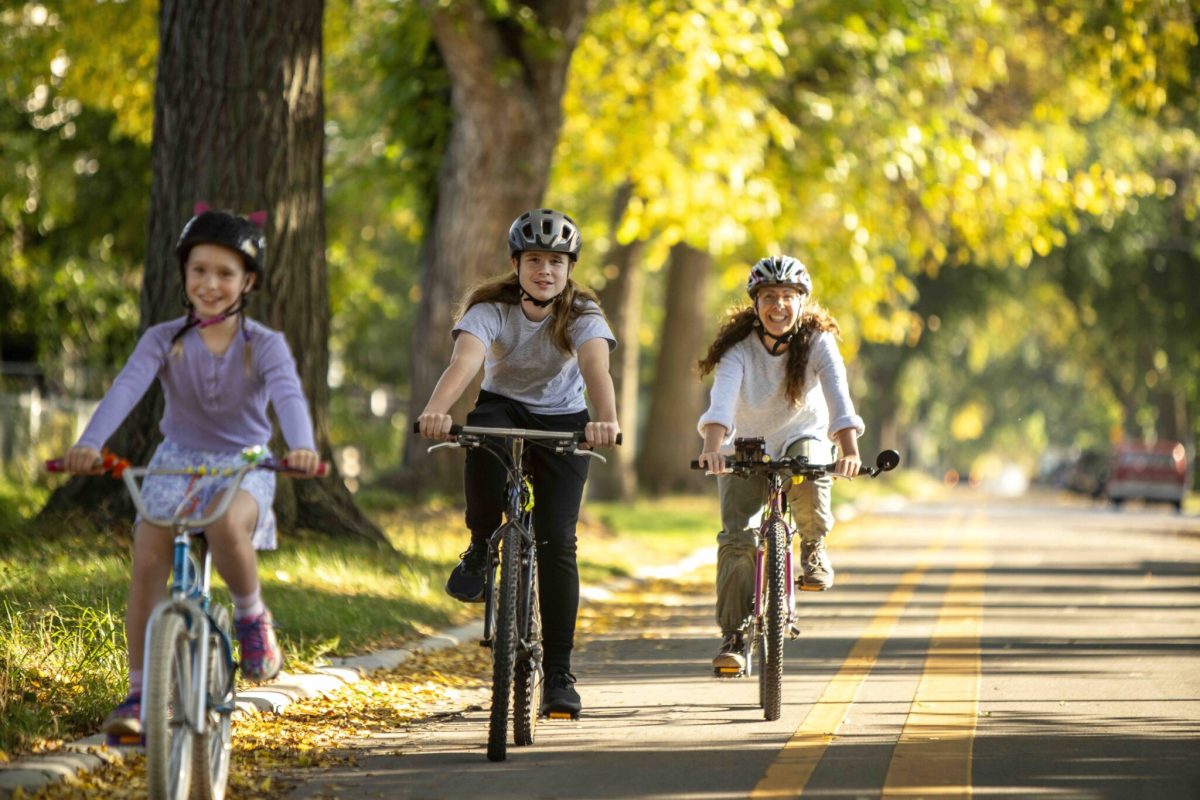 Three people biking in a row in a bike lane with on a tree lined street.