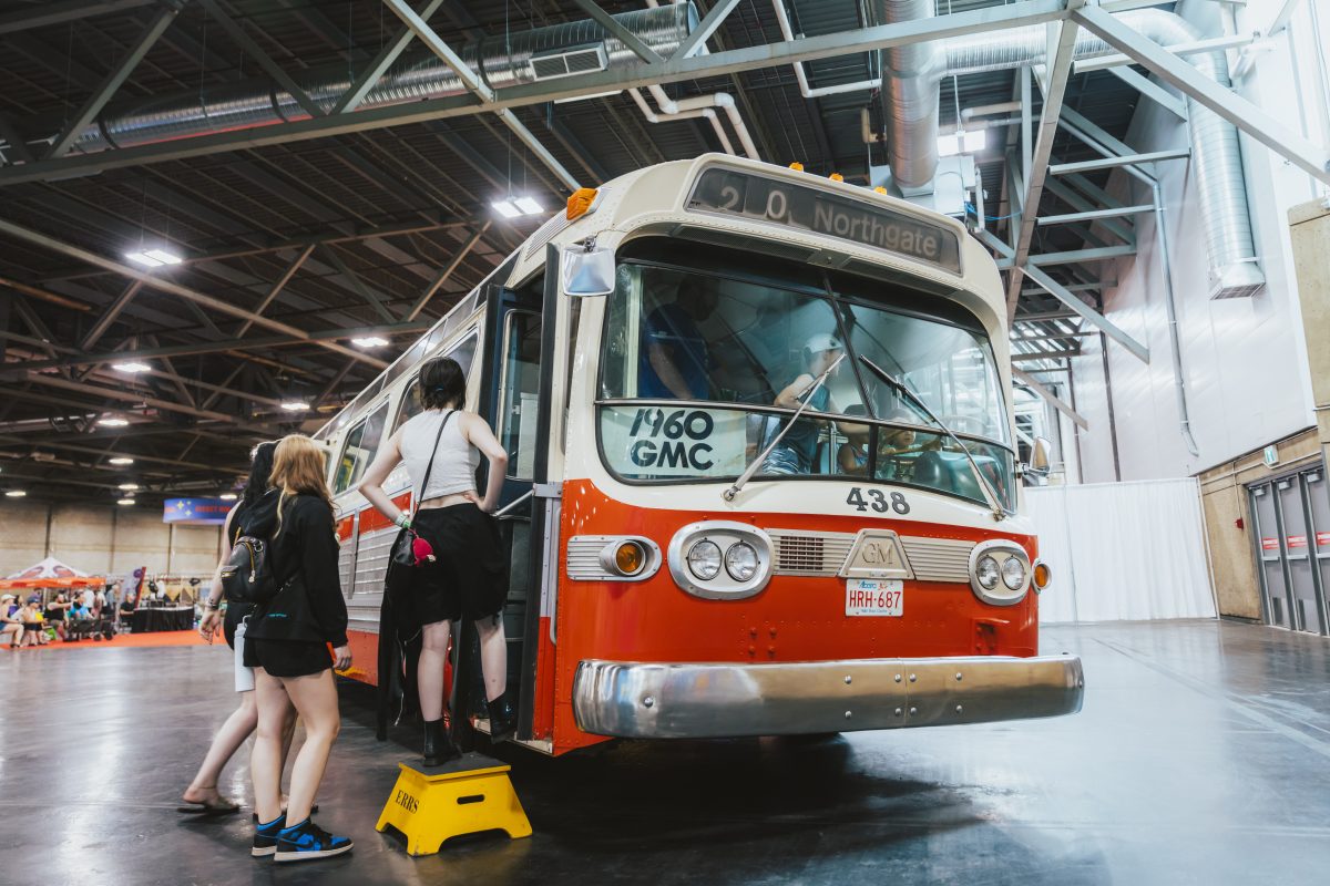 Three people waiting to board a vintage bus at an exhibit.