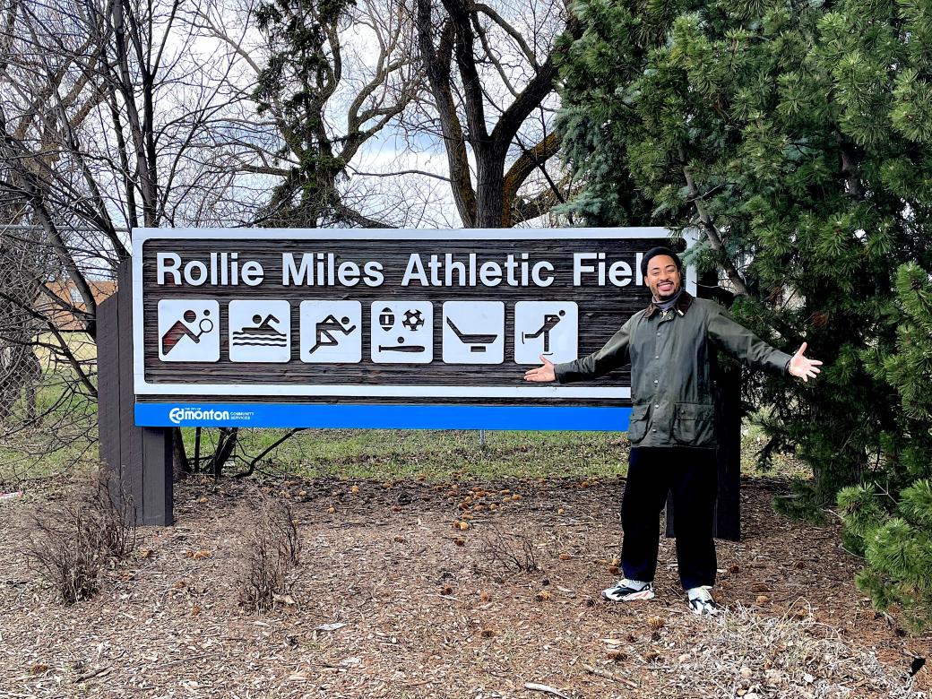 Rollie Pemberton stands in front of a sign for Rollie Miles Athletic Field. 