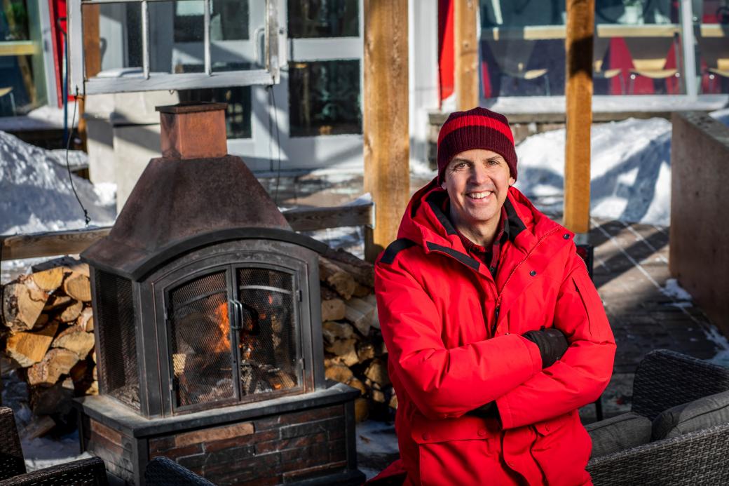Daniel Cournoyer poses in a red winter jacket in front of a fireplace on the Café Bicyclette patio in the winter. 