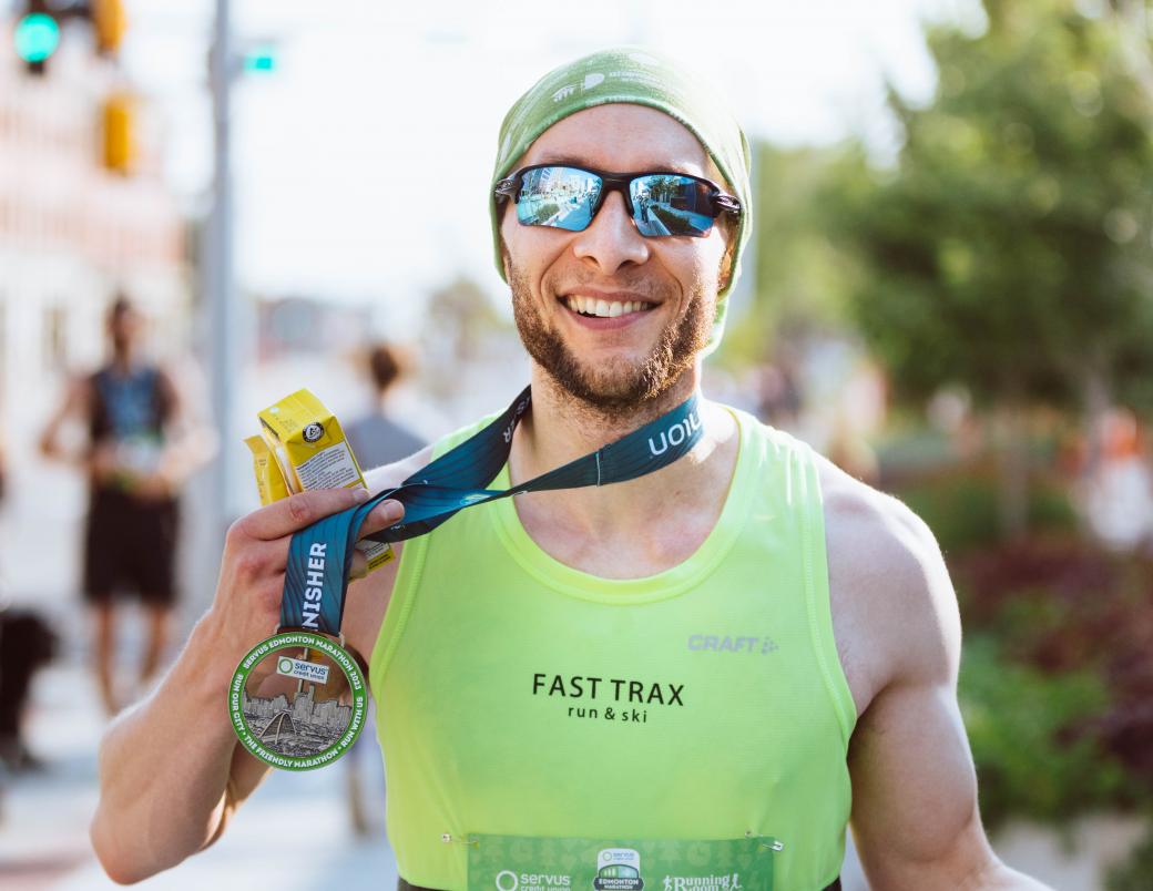 A smiling man wearing sunglasses holds up a medal hanging around his neck. 