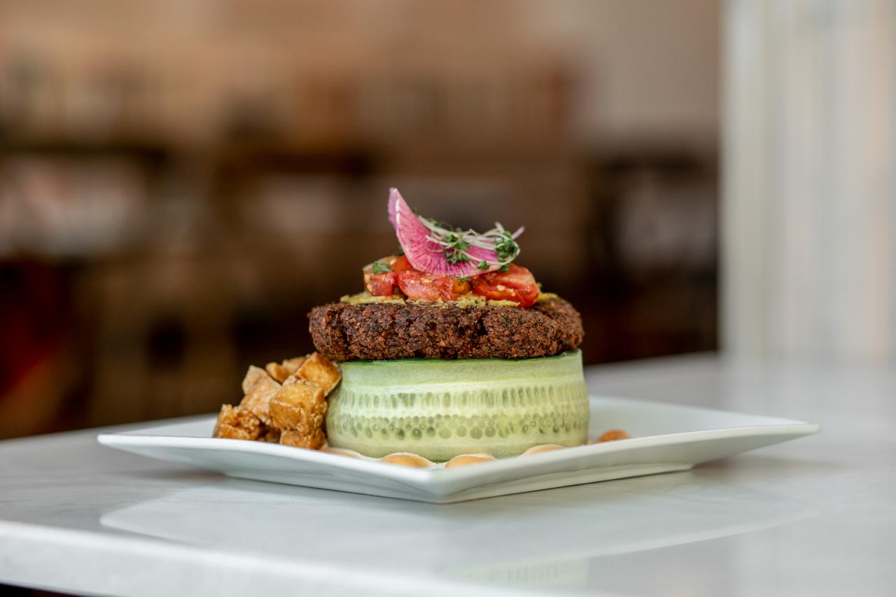 A vegetarian stacked meal presented on a plate includes a cucumber, patty, tomatoes and onions. 