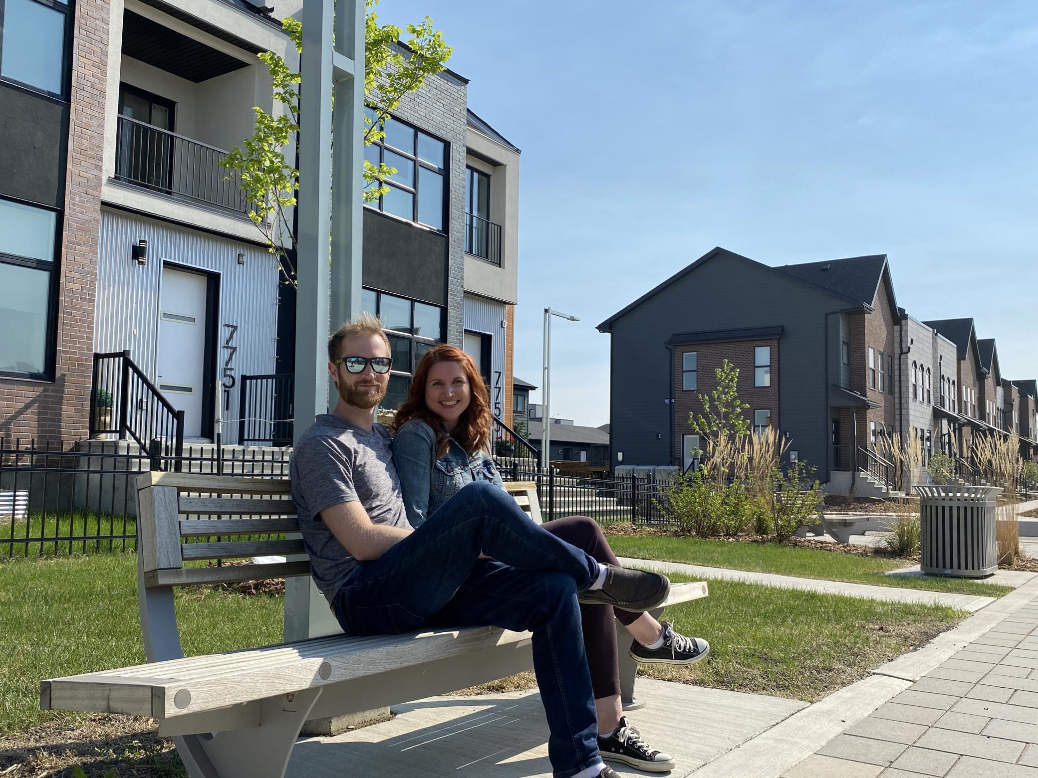 A couple sitting on a bench in front of homes