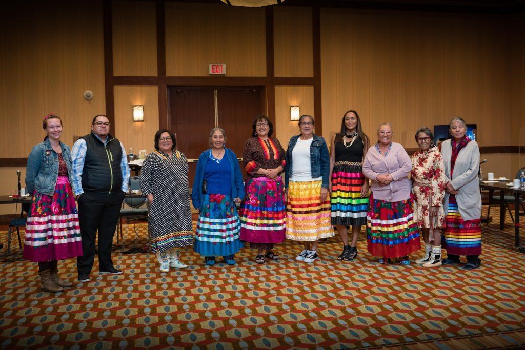 Ten indigenous leaders, mostly women in colourful skirts, stand in a meeting room. 