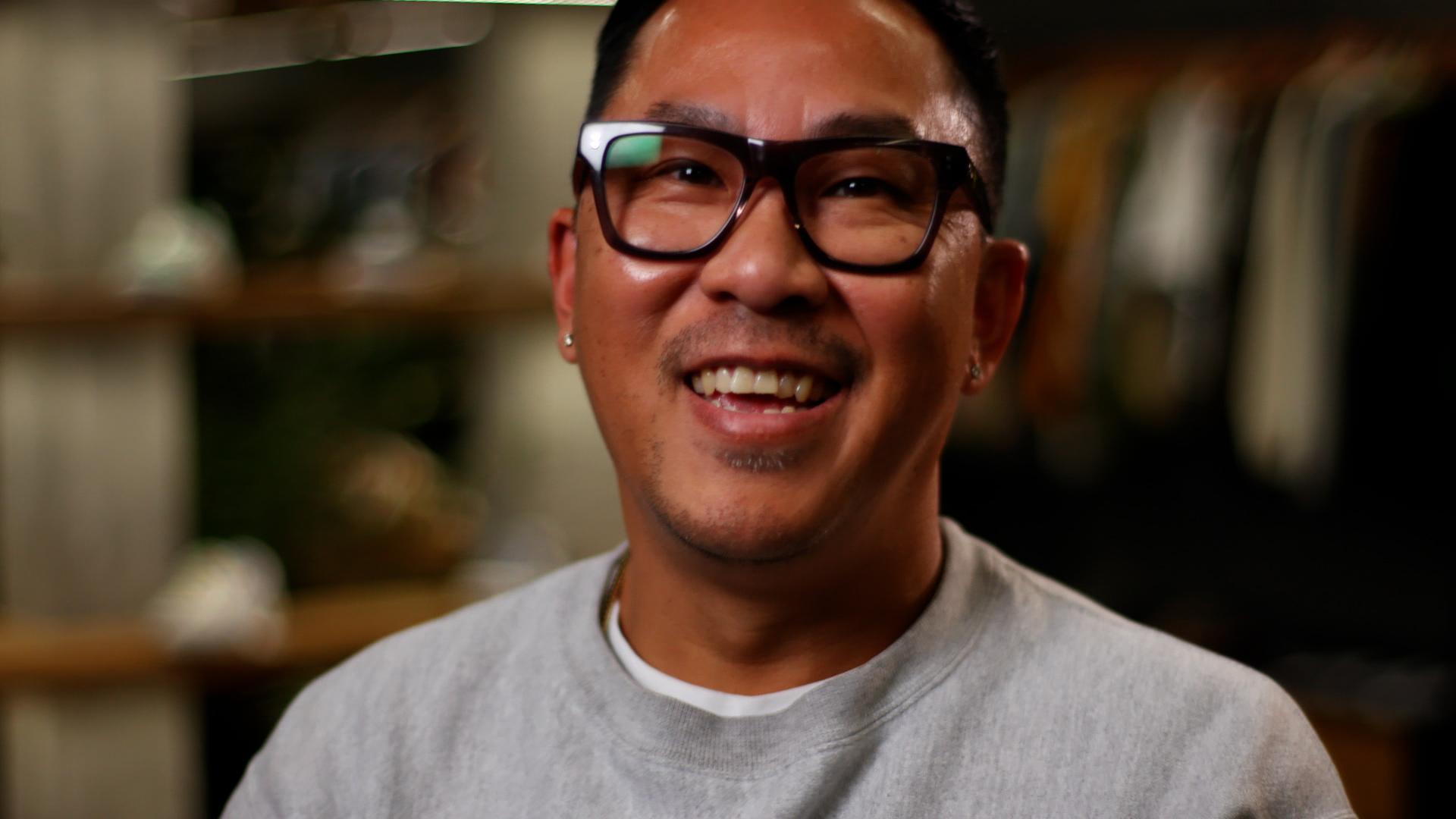 A man wearing thick black rimmed glasses laughs towards the camera.