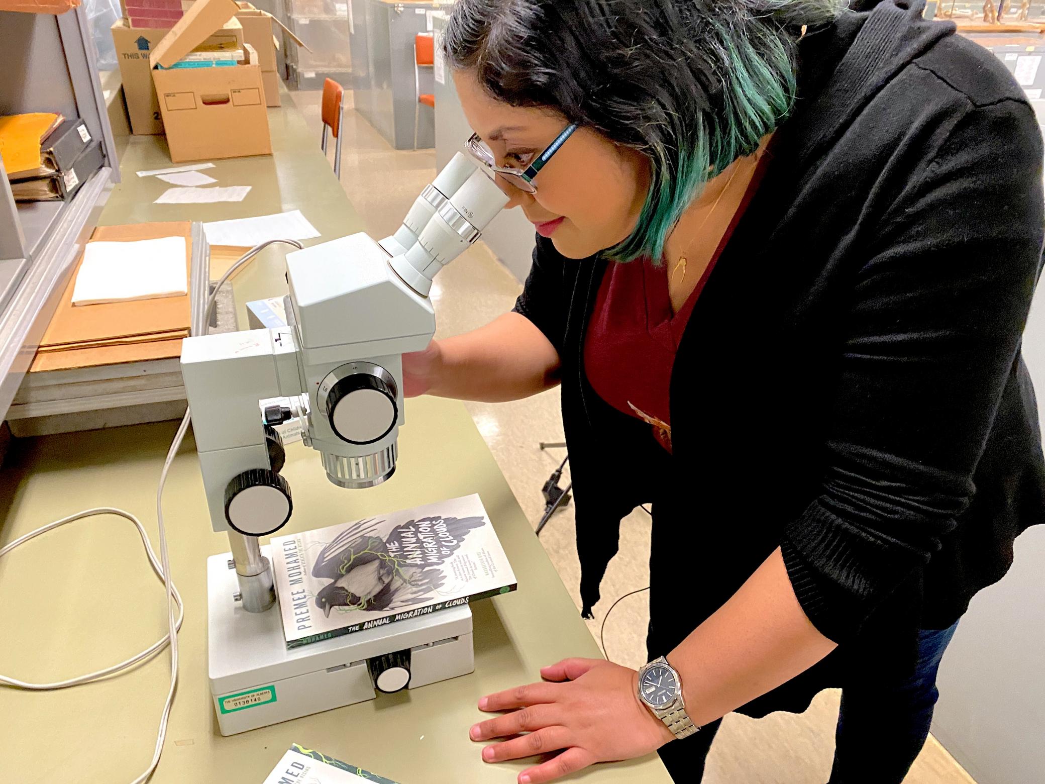 Author and scientist Premee Mohamed looks into a microscope in a lab.