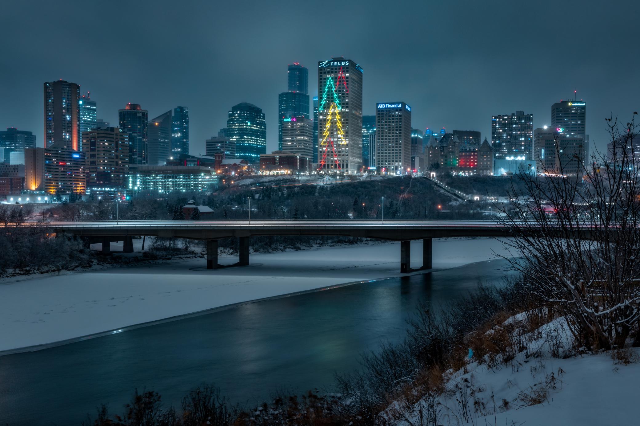 View of the Edmonton downtown skyline at night in the winter. The Christmas trees installation on the Telus building are lit up in red, green and yellow.