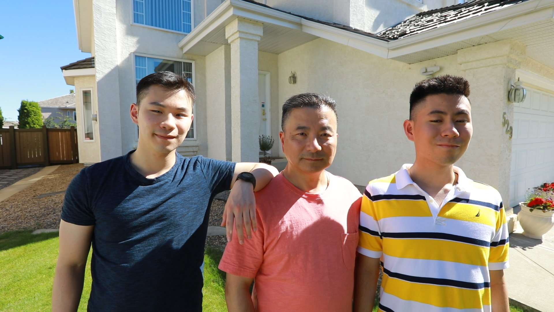 Three men, a father in between his two sons, stand outside in front of a house. 