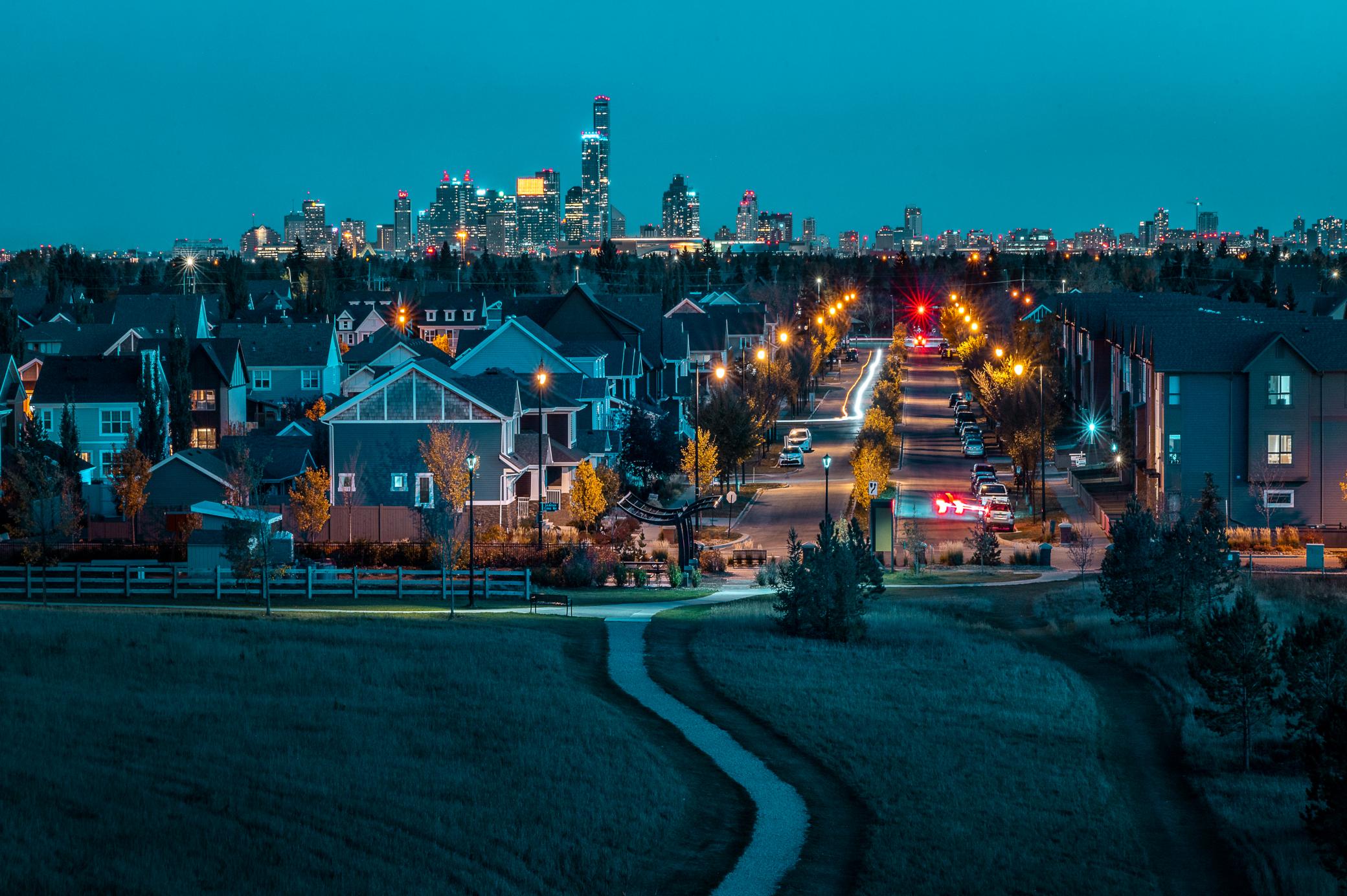 A neighbourhood and park with a trail in front and the downtown skyline in the distance.