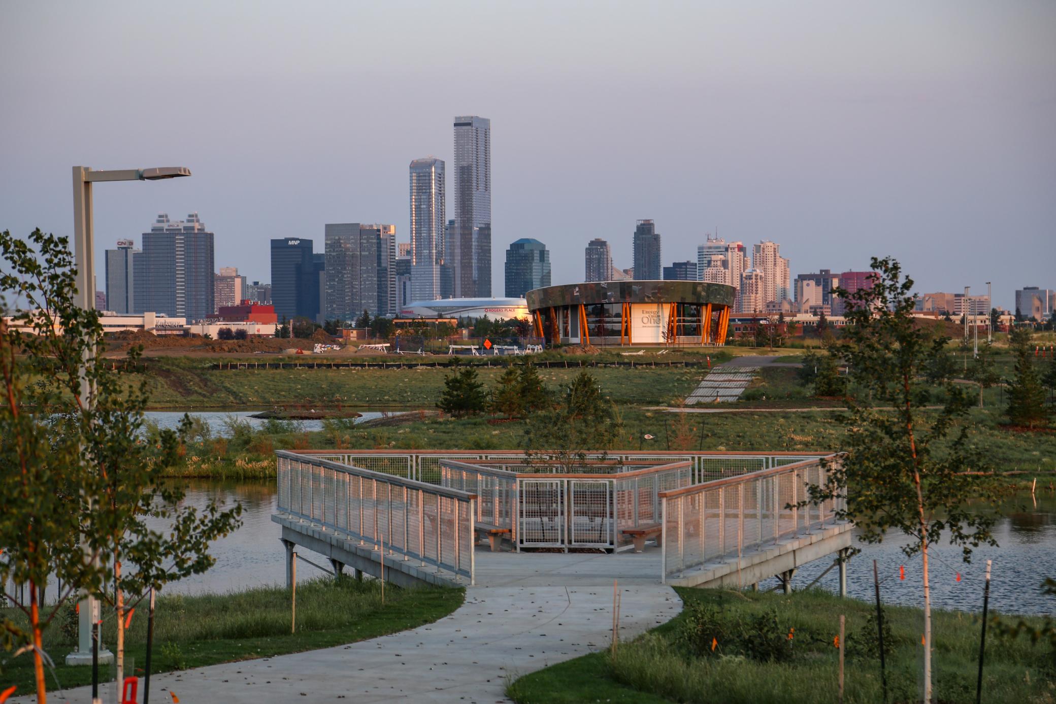 Lookout over a pond with an energy center building and downtown Edmonton skyline behind it at sunset.