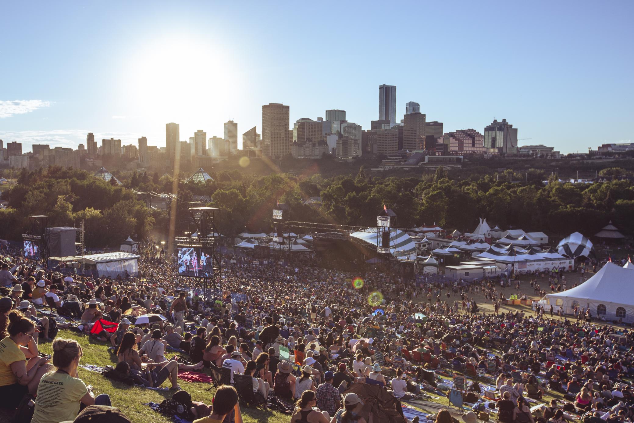 With downtown Edmonton’s skyline as a backdrop, hundreds of people sit on the grassy slopes of Gallagher Park, watching a musician perform on the Folk Fest’s stages.  