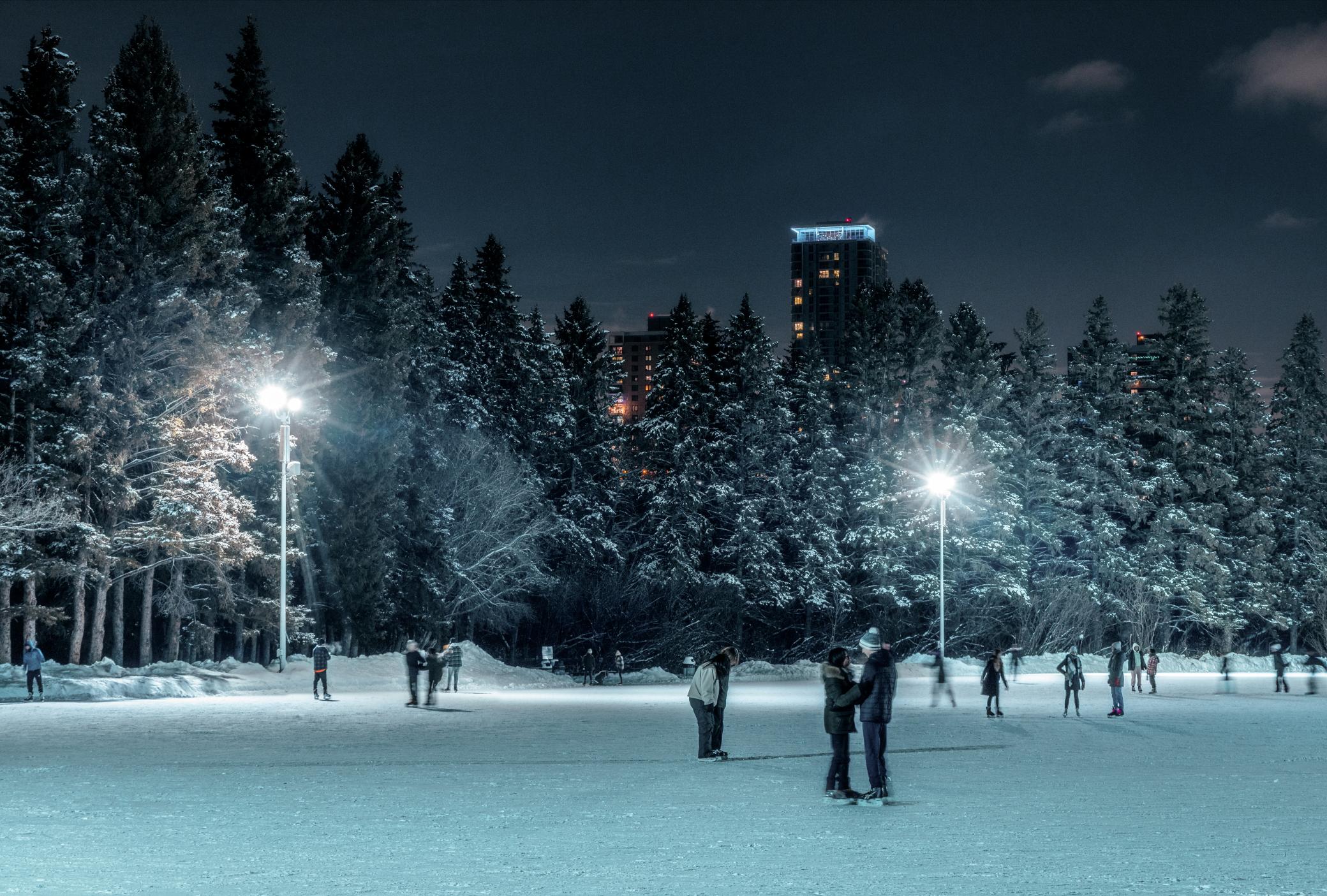 People skating at the victoria park oval at night in the winter.
