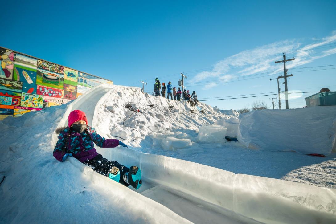 A close up of a child sliding down a giant ice slide with a blue sky in the background.