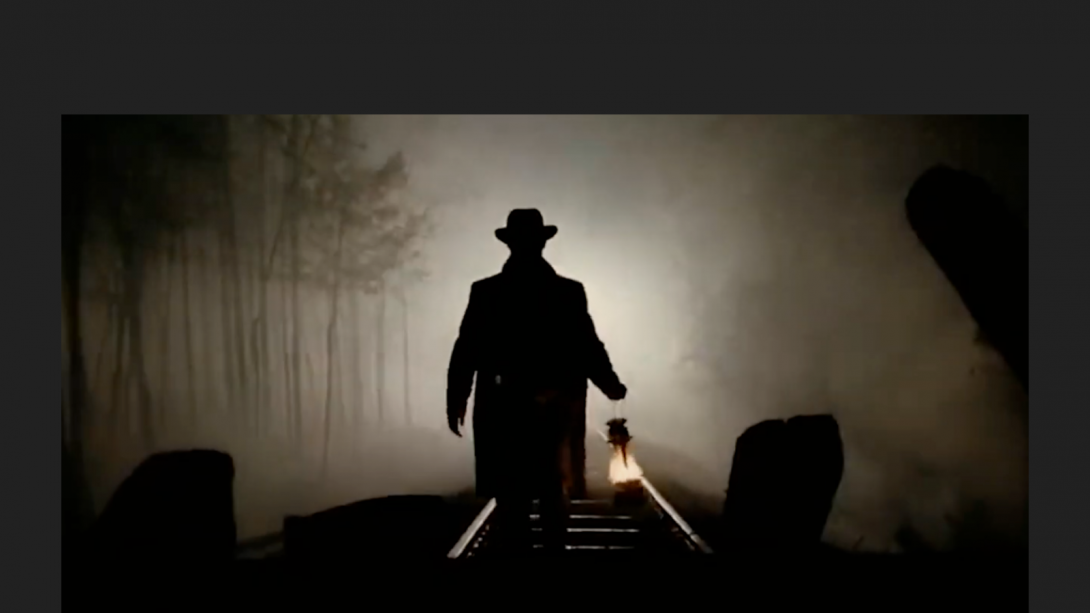 A movie screenshot of a shadow of a man holding a kerosene lamp walking away on railroad tracks. 