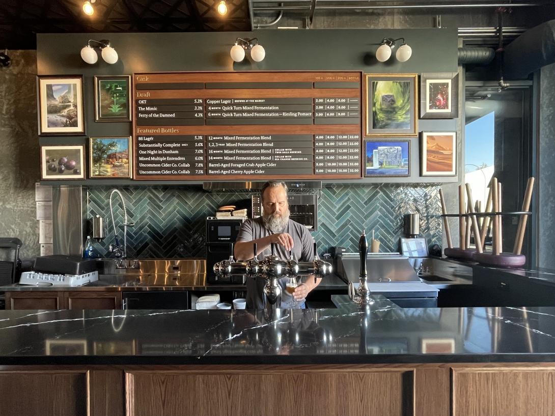 A man pours a glass of beer behind the counter of a taproom.