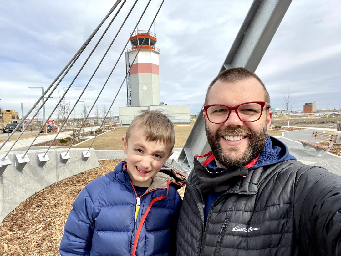 Father and son photo with Blatchford Control Tower in the background with overcast skies above.