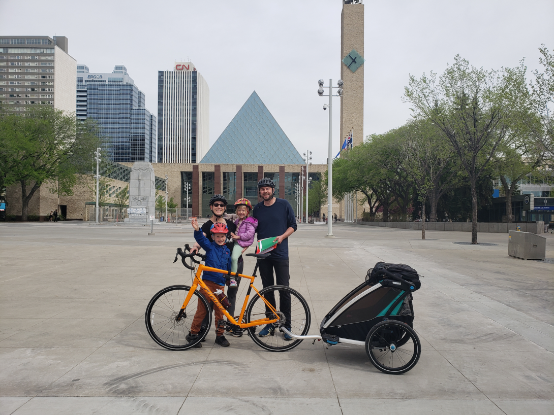 Sean Collins with his wife and 2 kids stand by a bike with a trailer in Sir Winston Churchill Square.