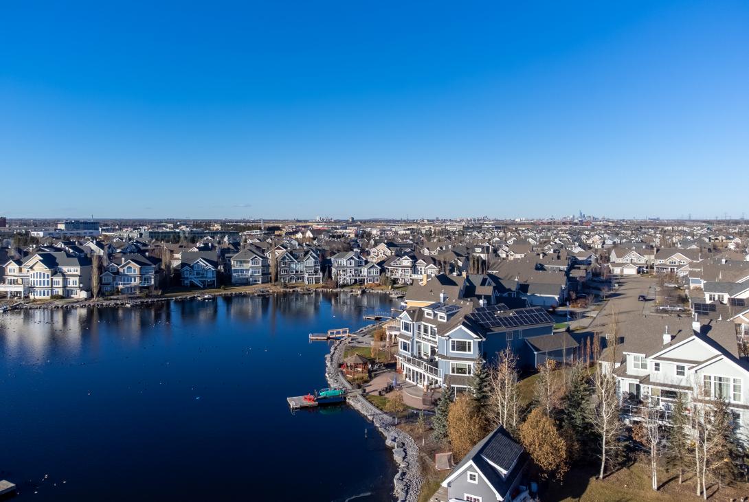 Homes line the perimeter of a lake as a cloudless blue sky shines above. 