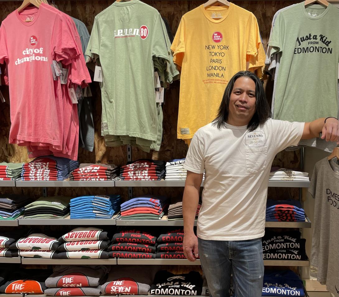 Ador Cochingco stands in front of his Seven80 t-shirts that are hanging and folded behind him.
