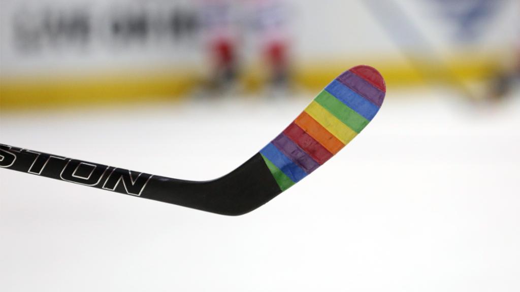 A close up of hockey stick with rainbow tape.