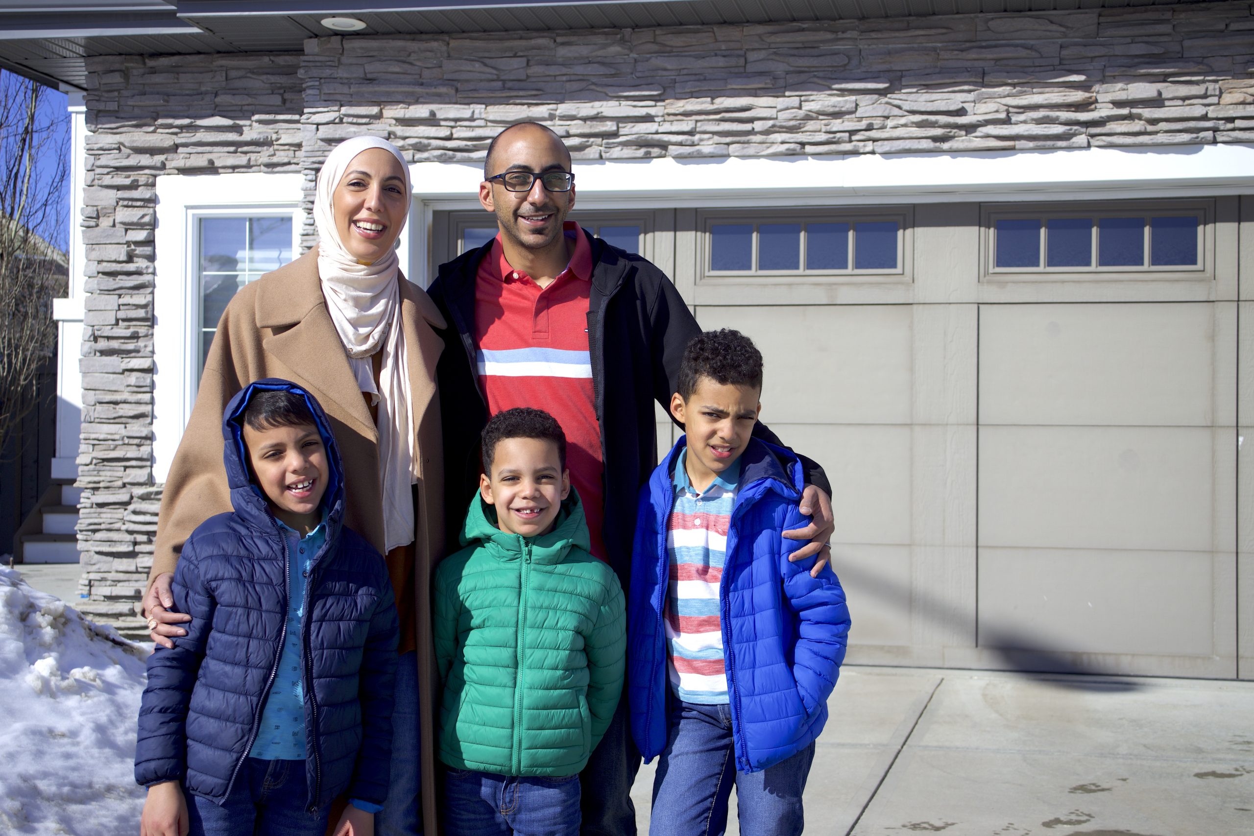 Parents and their three children stand outside their home in the winter.