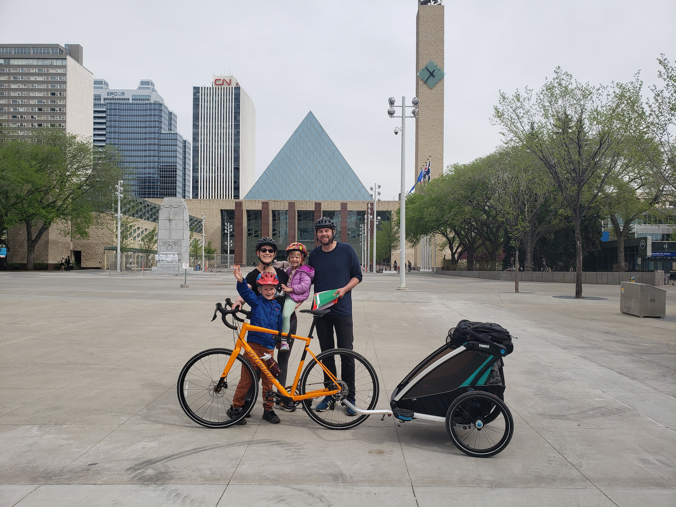 Sean Collins with his wife and 2 kids stand by a bike with a trailer in Sir Winston Churchill Square