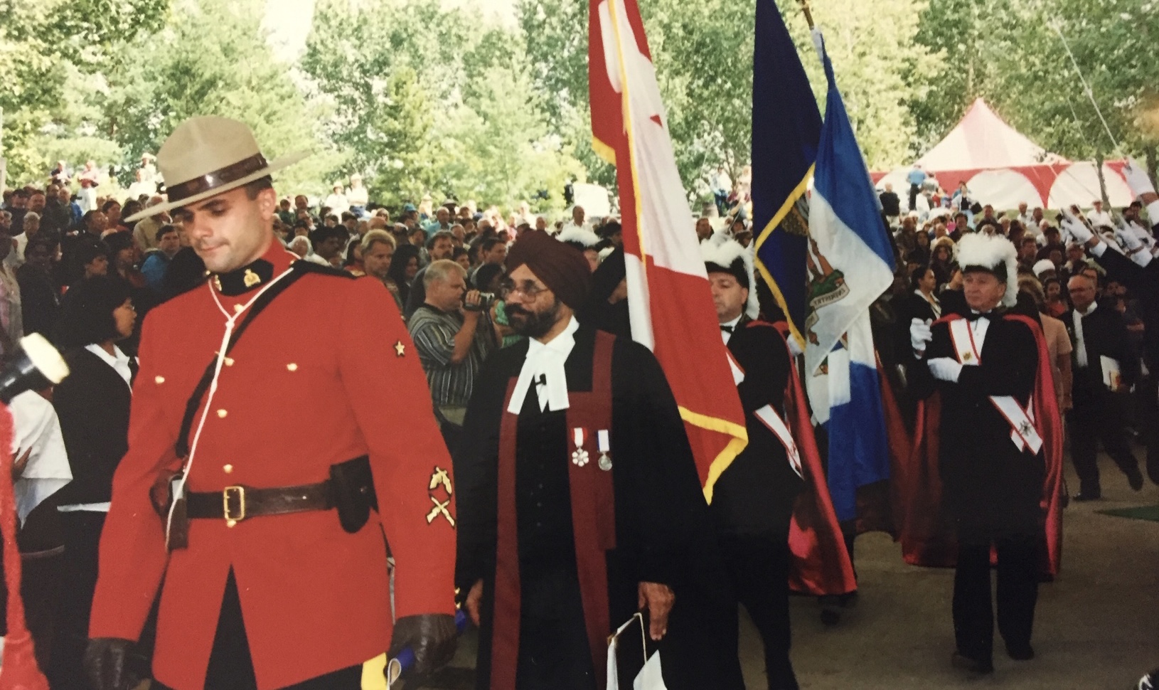 A judge in robes is part of a Canadian citizen ceremony, with flags and a Mountie in the background.