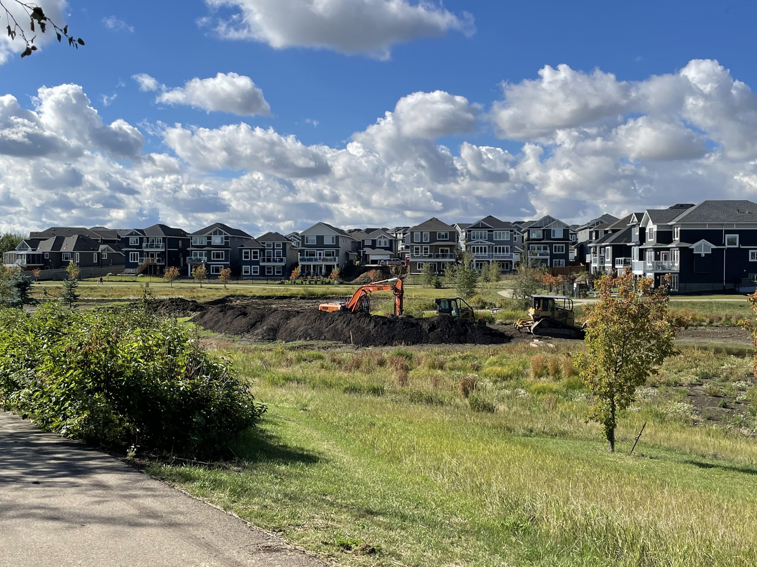 Construction vehicles dig in a field with new houses in the background.