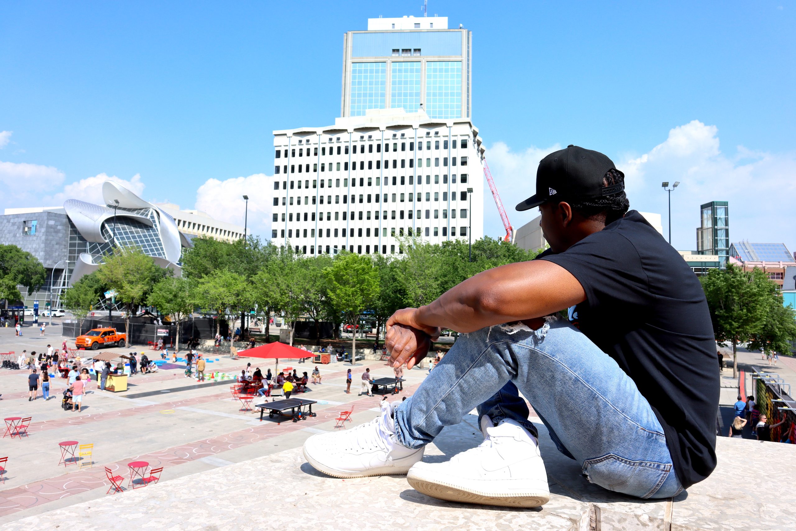 A man in jeans and black tshirt sits to the right of of the frame with a square pavillion to his right.