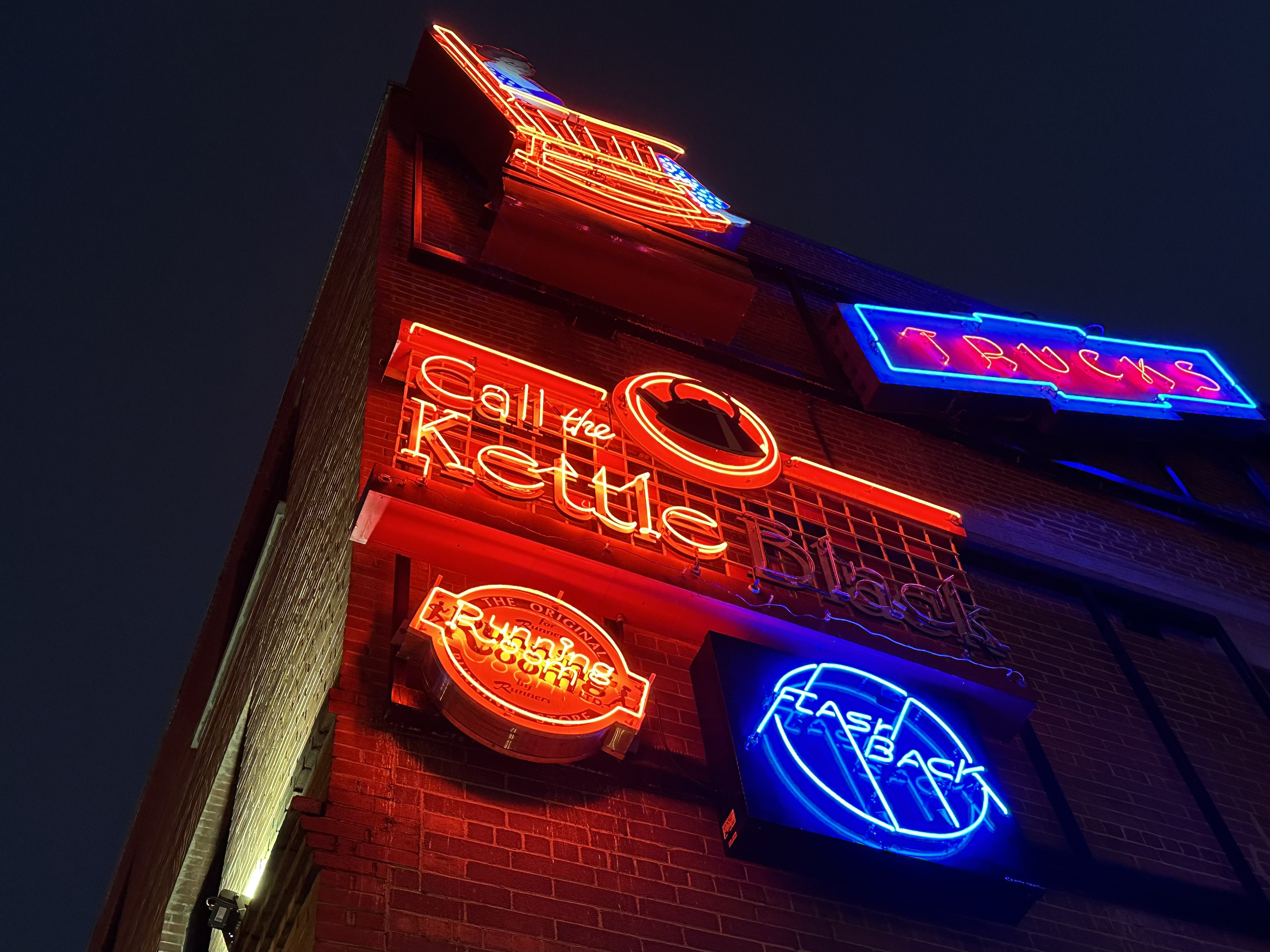 Several lit neon signs hang on a brick wall