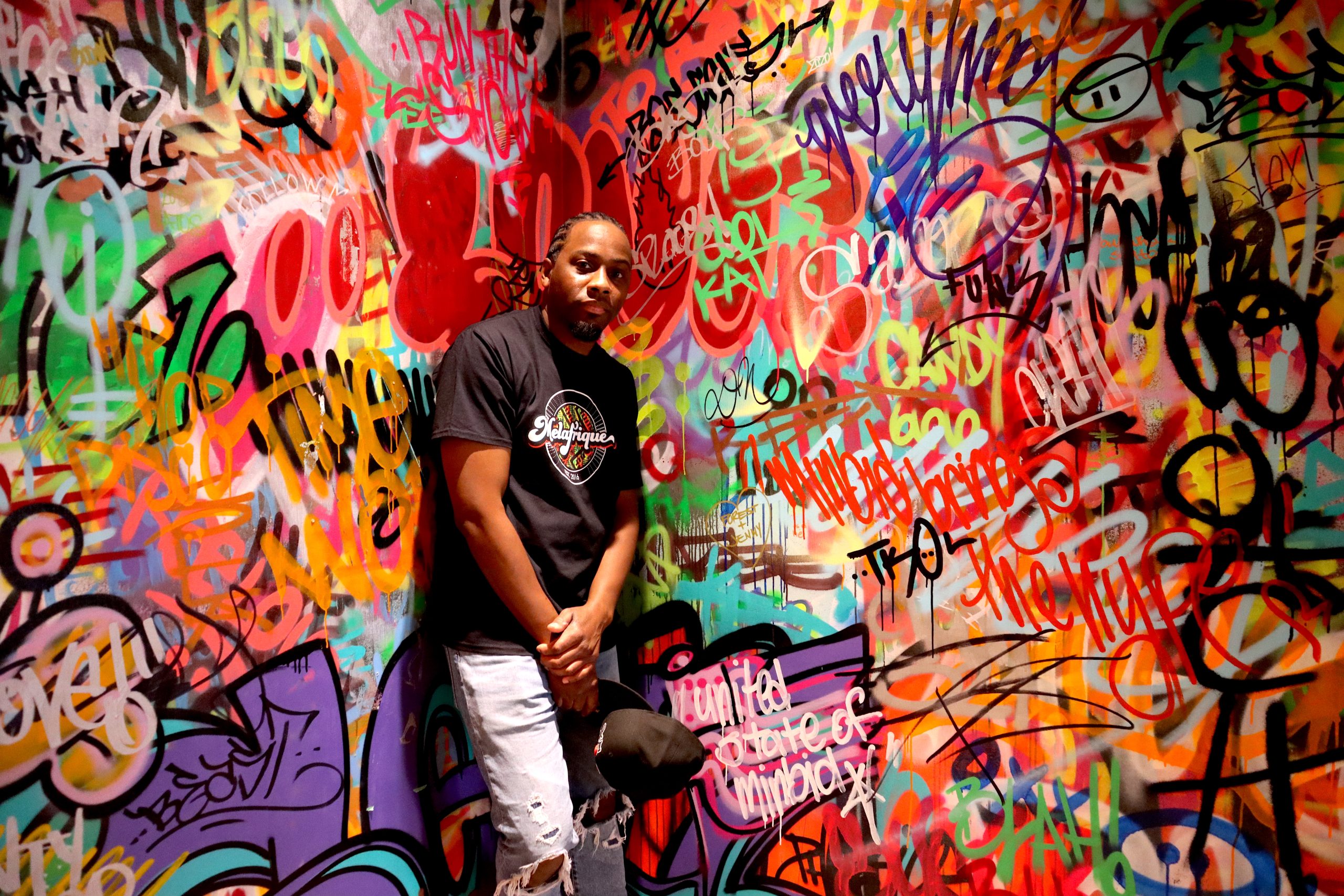 A black man stands in the corner with colourful graffiti covering the walls,