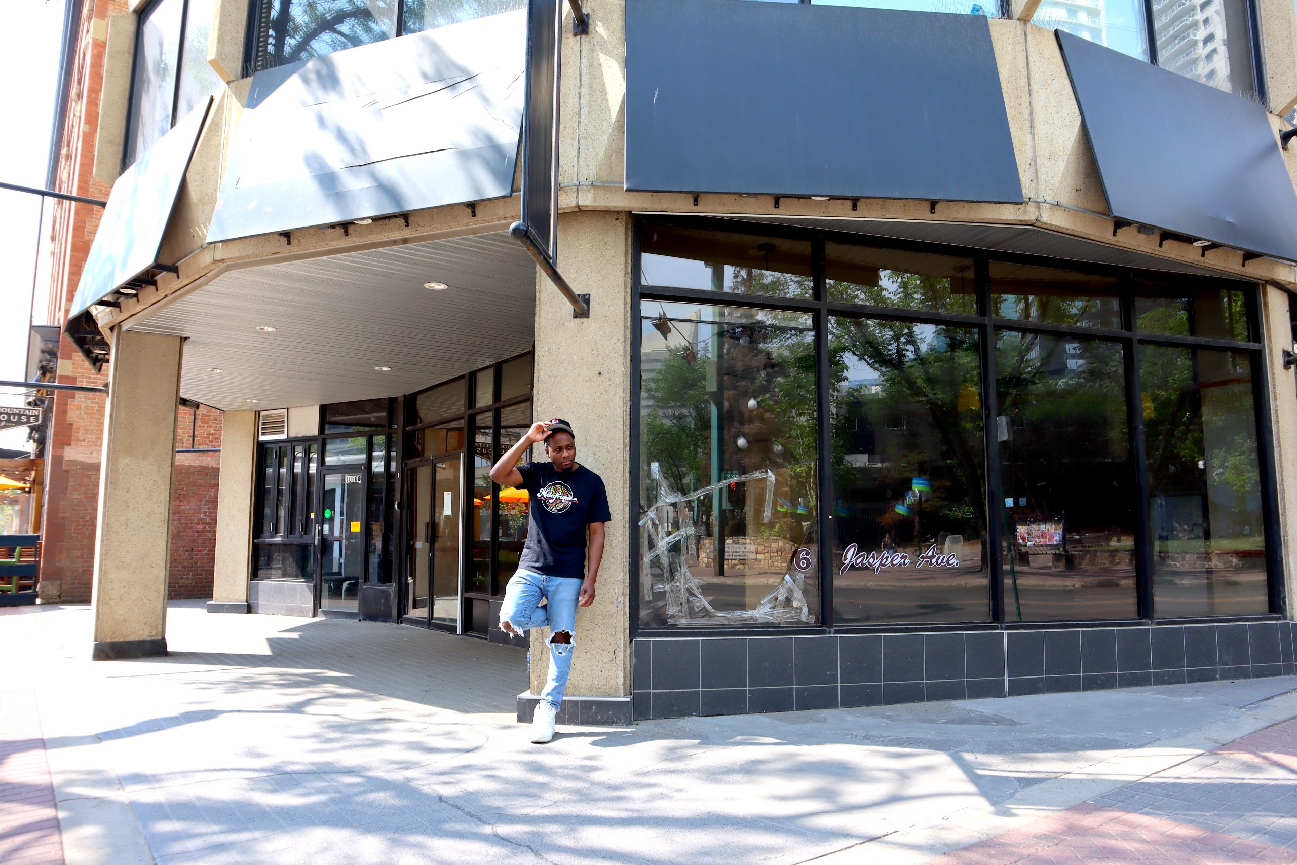 black man leans against a pillar outside a building corner.