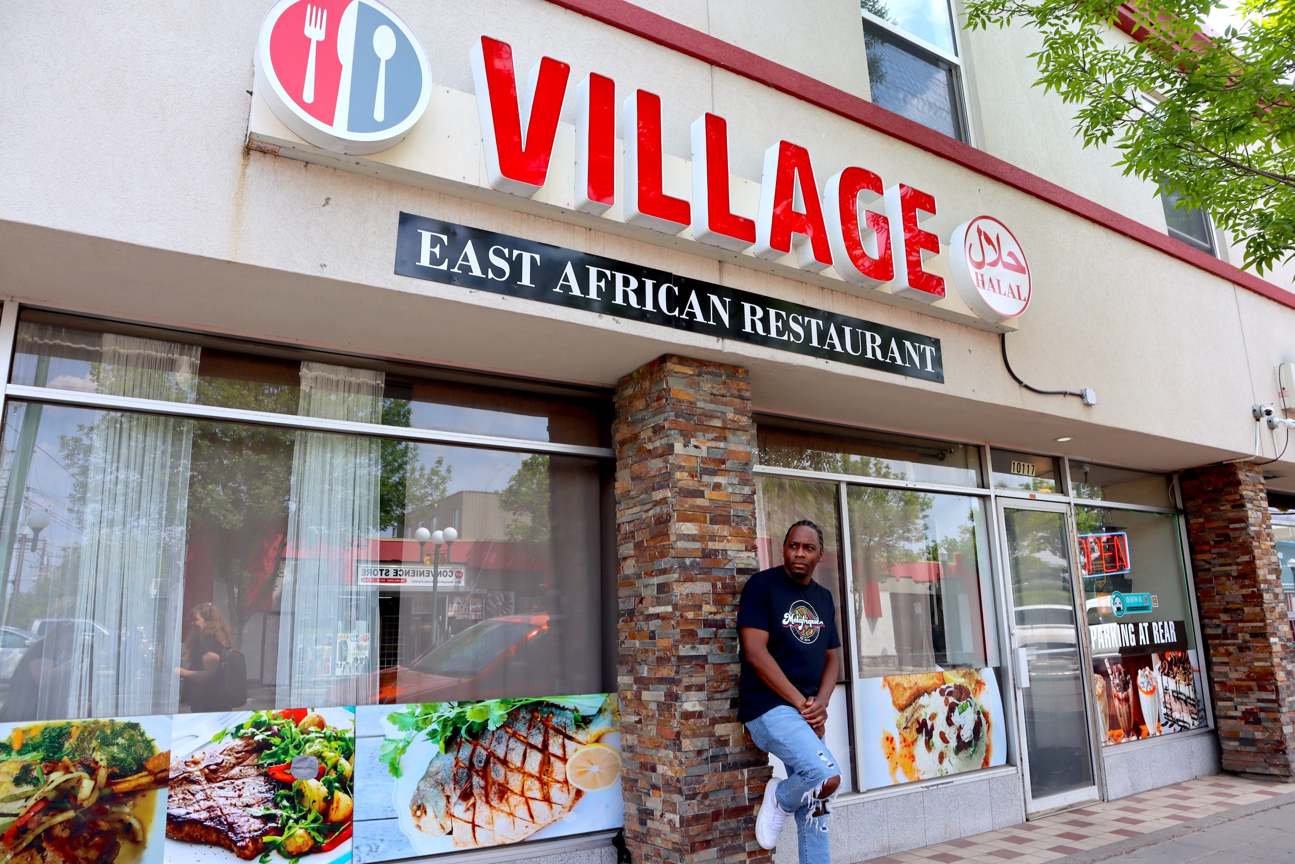 A man leans against a pillar outside a restaurant.