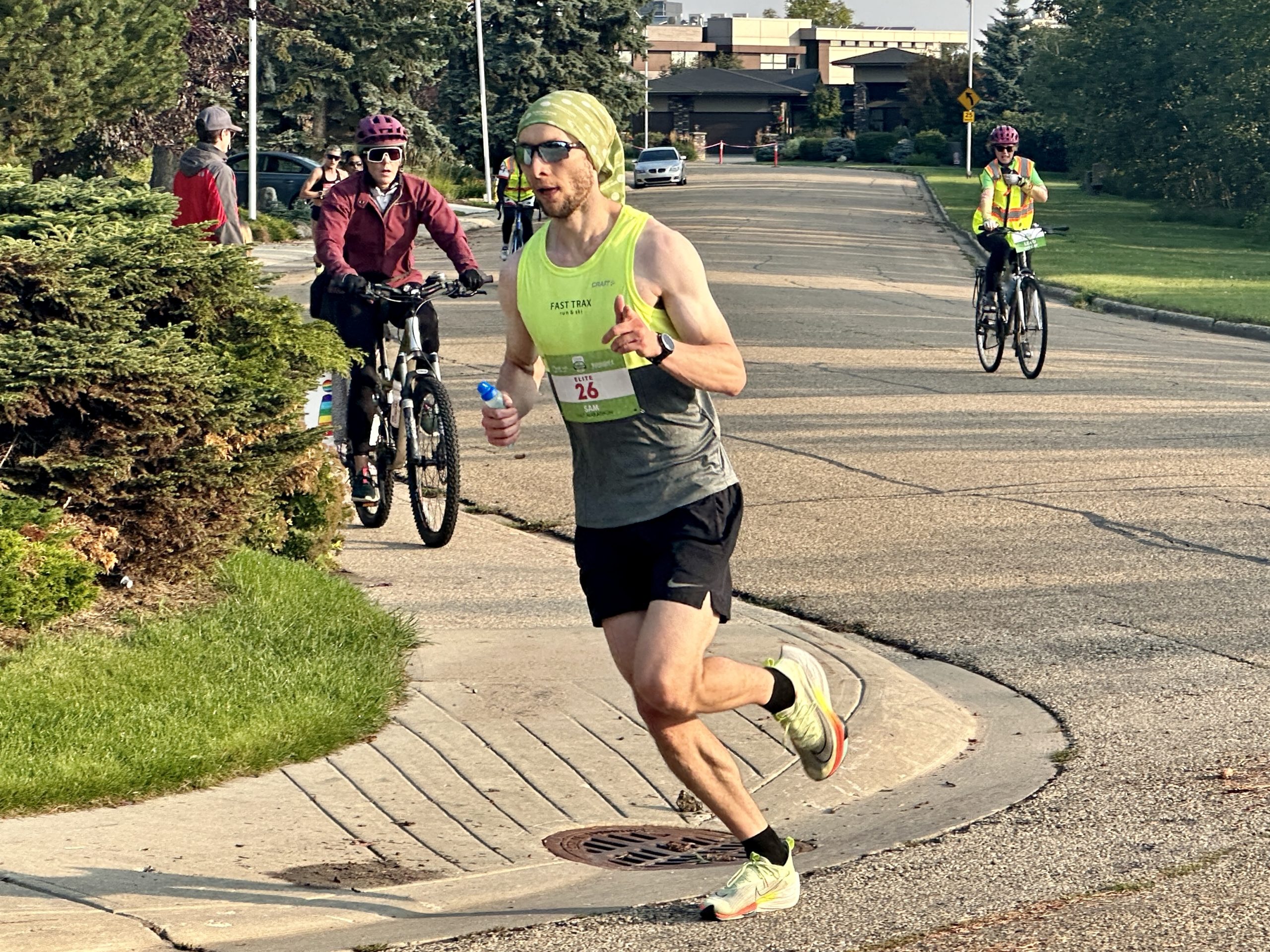 A runner rounds the corner on a street as he races in the Edmonton Marathon, followed by two people on bicycles.