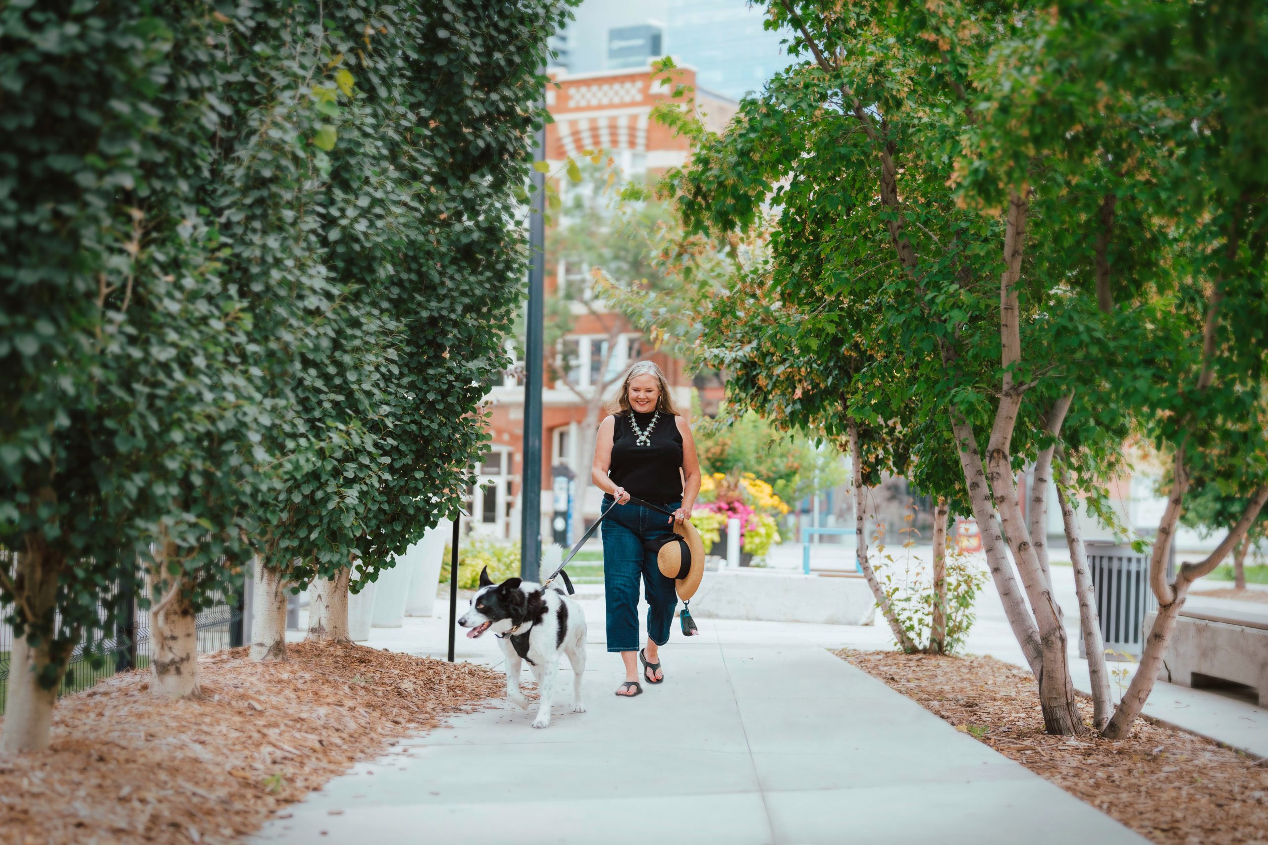 A woman, holding a hat, walks her dog through a tree-lined path. Credit: City of Edmonton