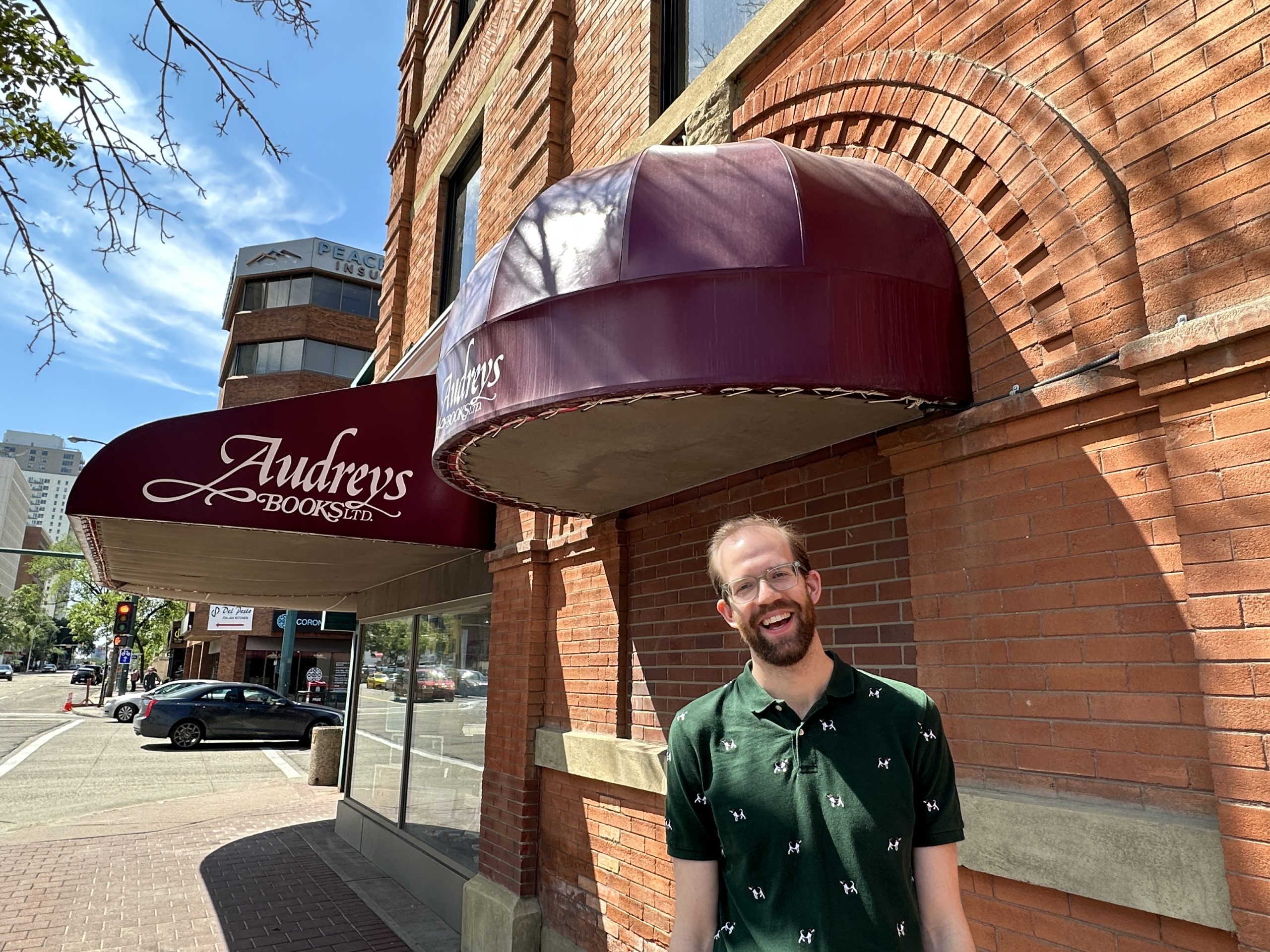 A smiling man stands next to a book store in a brick building.