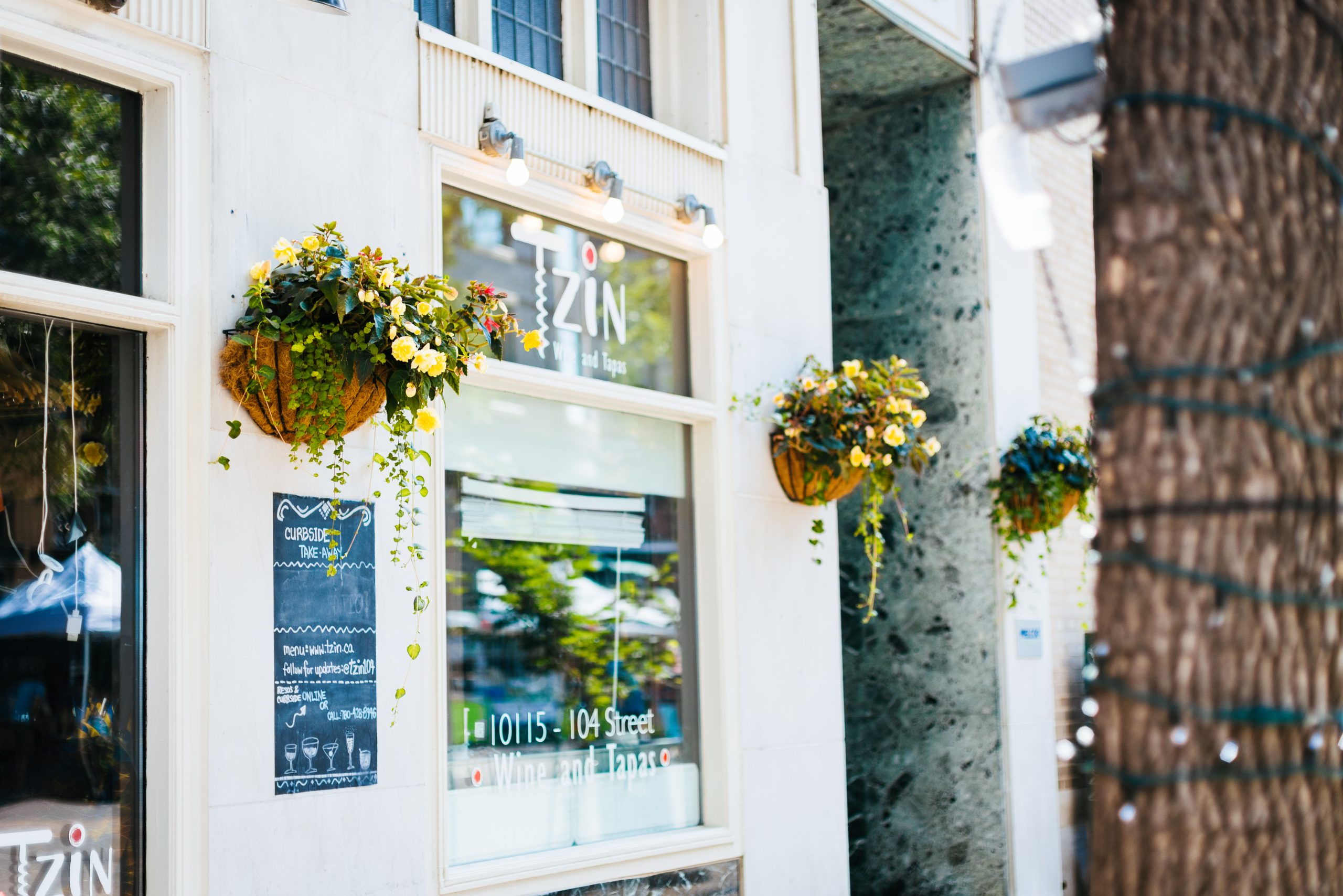 The front windows of a white building with three hanging floral baskets.