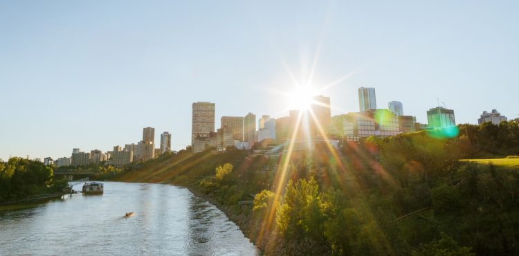 Edmonton downtown skyline summer with the North Saskatchewan River on the left. A sun burst is coming through the tall downtown buildings.