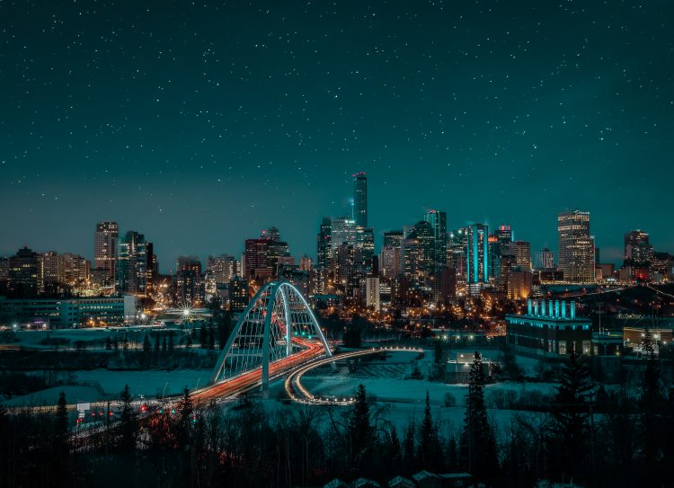 A view of a bridge, Edmonton’s downtown skyline, and stars in the night sky.