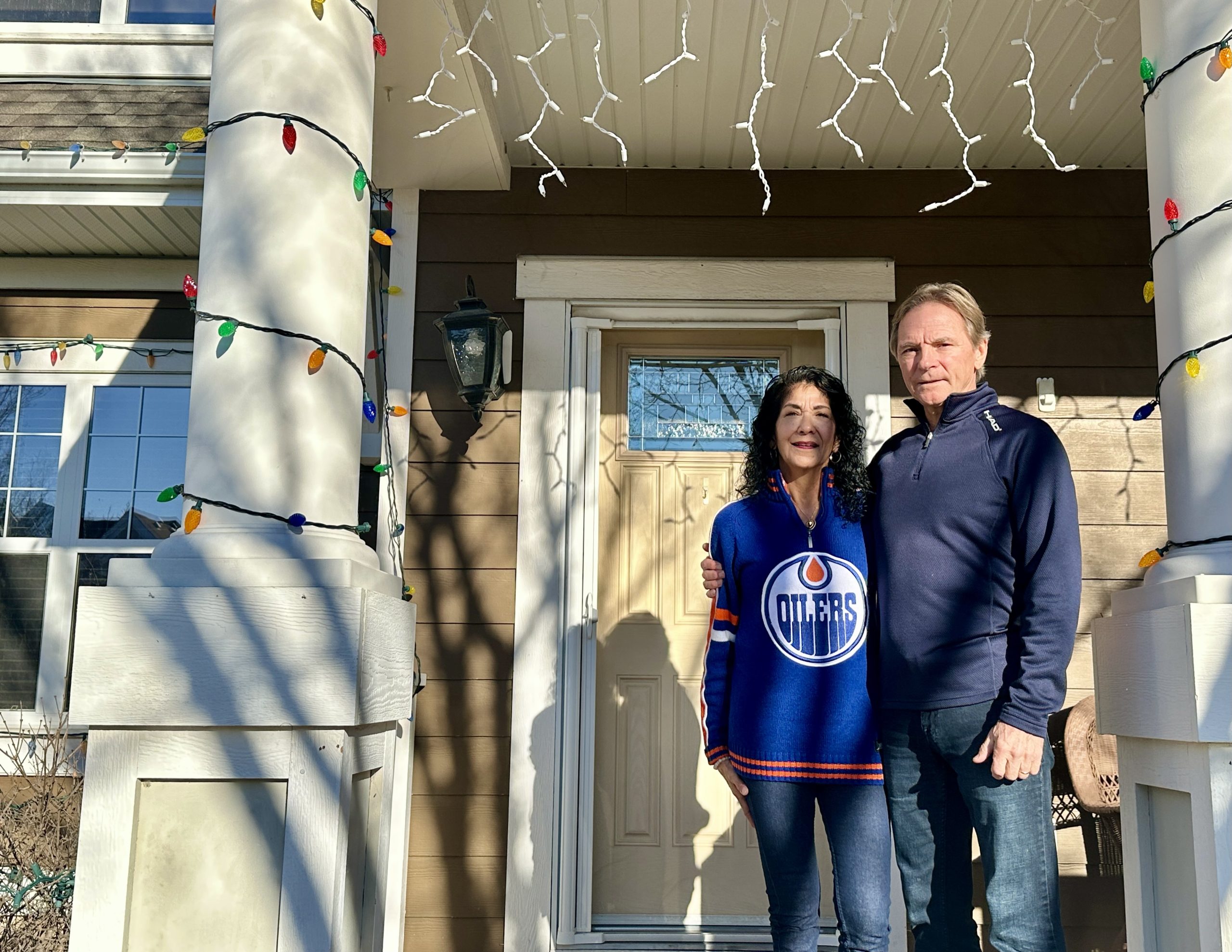 A man and a woman stand outside the front door of their house.