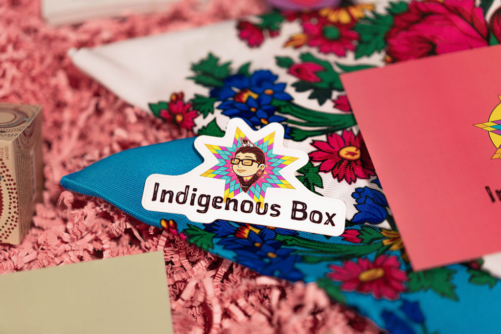 An Indigenous Box sticker sits on top of a scarf decorated with flowers.