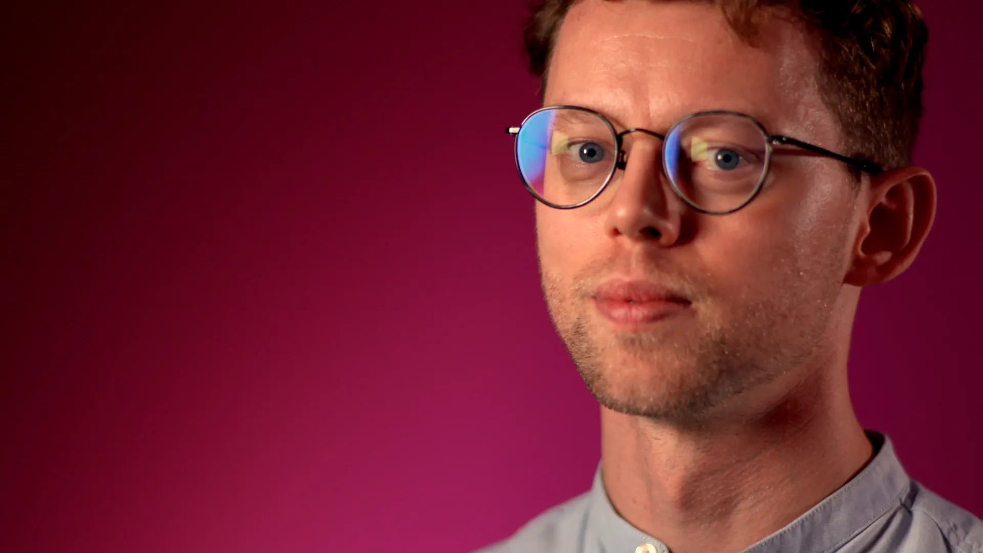 A man with glasses looking at the camera with a deep red background.