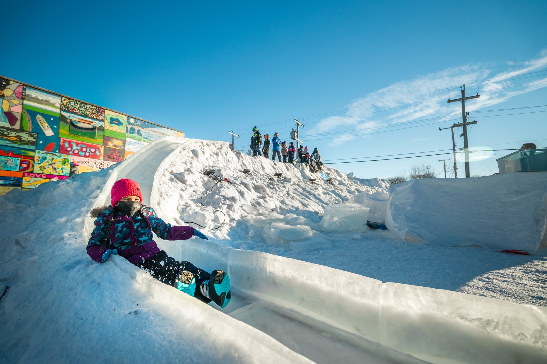 A close up of a child sliding down a giant ice slide with a blue sky in the background. Credit: Courtesy of Brandon Mattice/Explore Edmonton.