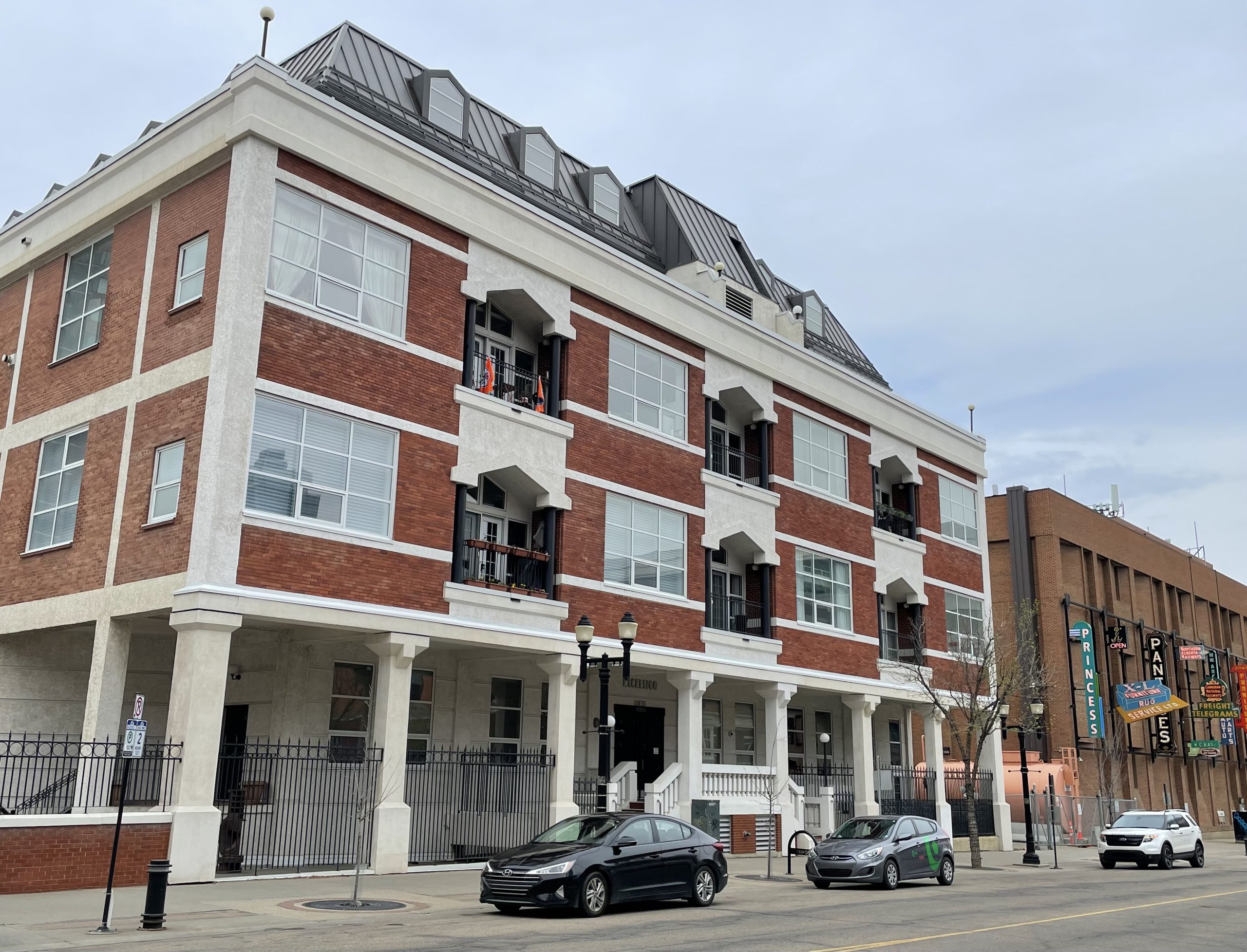 Three cars are parked in front of a brick condo building.