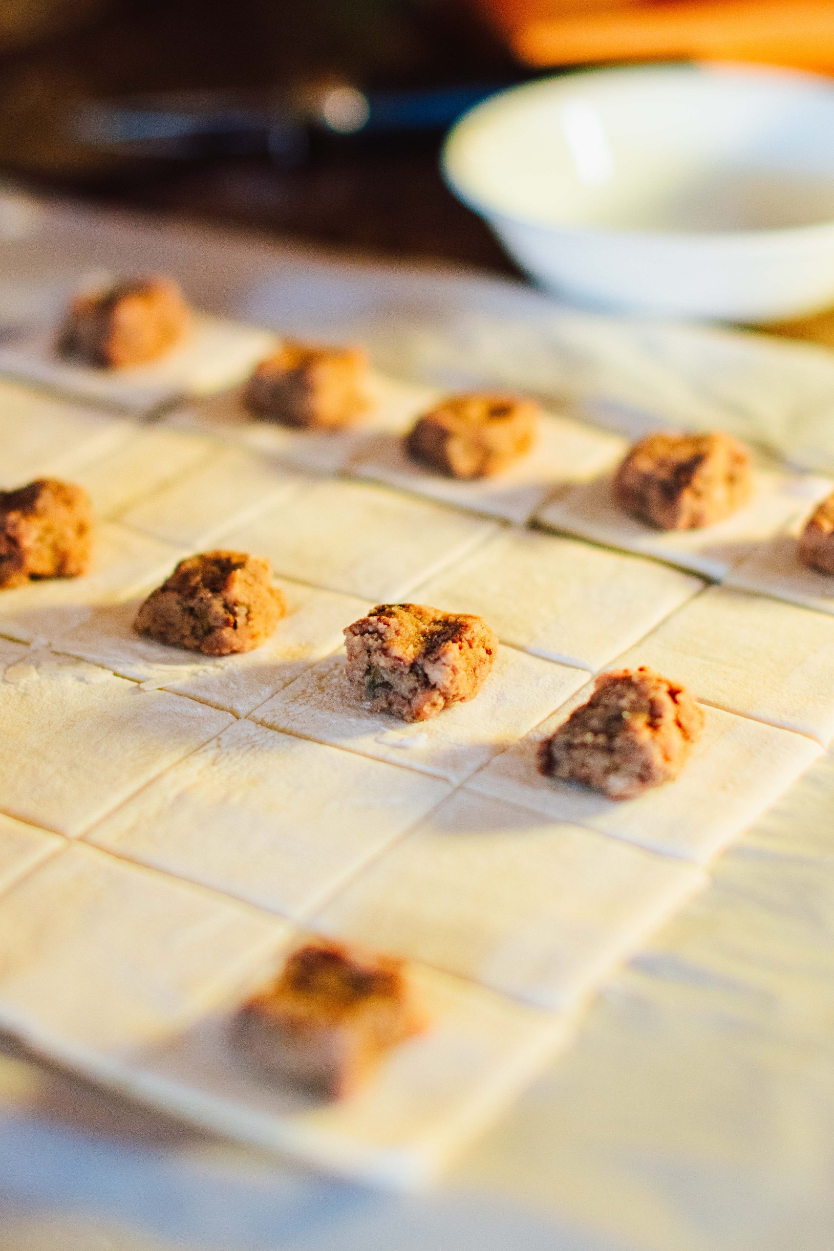 Close-up of neatly assembled uniform round balls of meat filling on squares of dough.