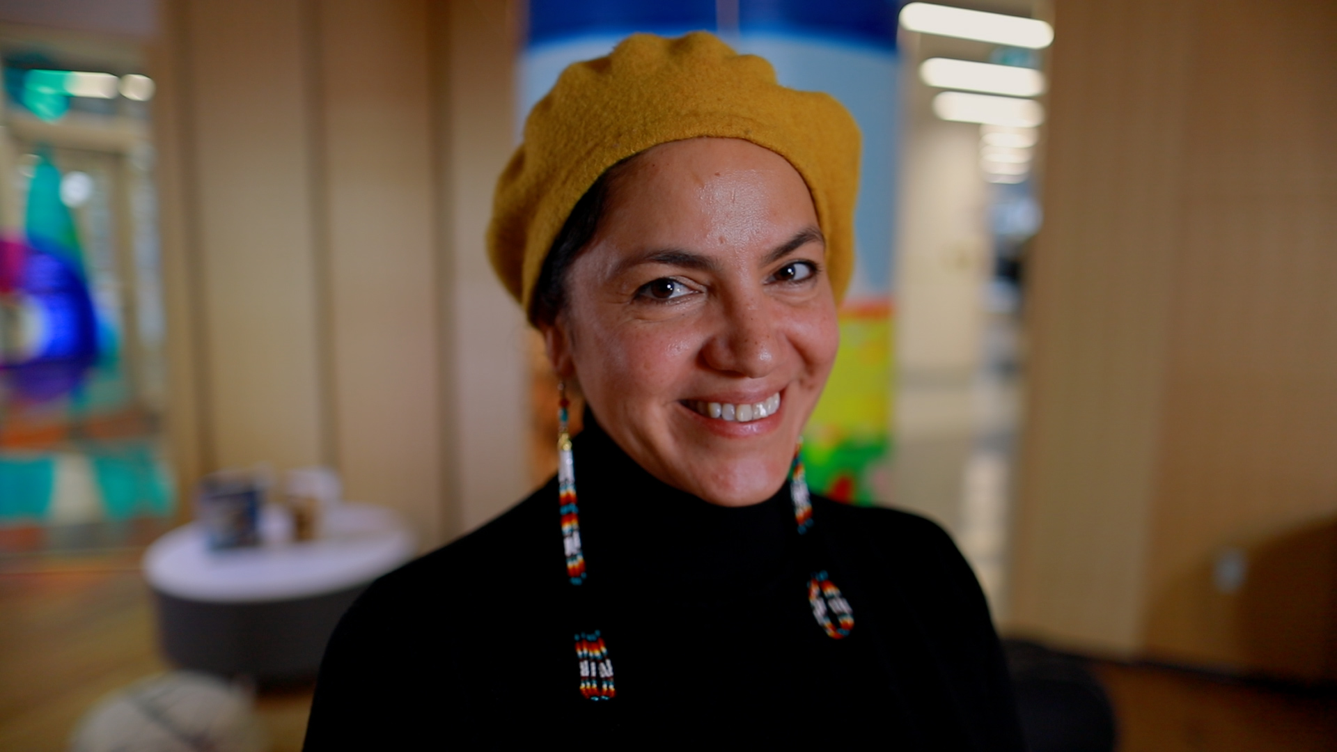 A woman in a yellow hat and black shirt smiles at the camera