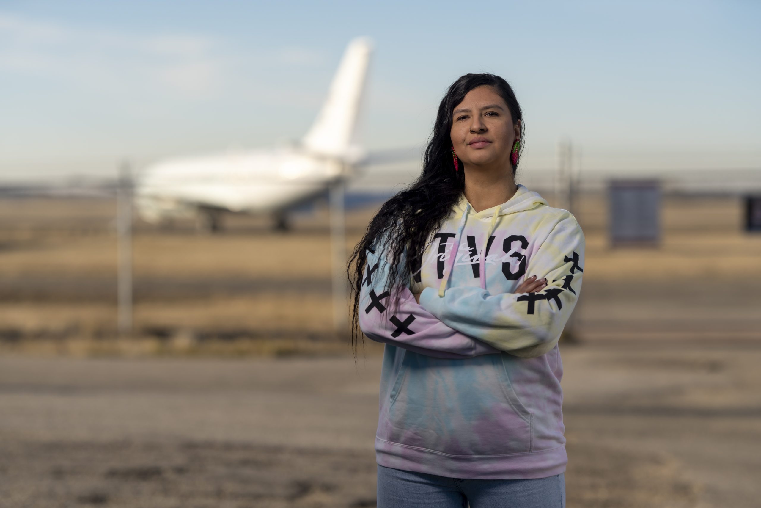 A woman with her arm crossed stands in front of a fenced-off airplane at the Edmonton International Airport.