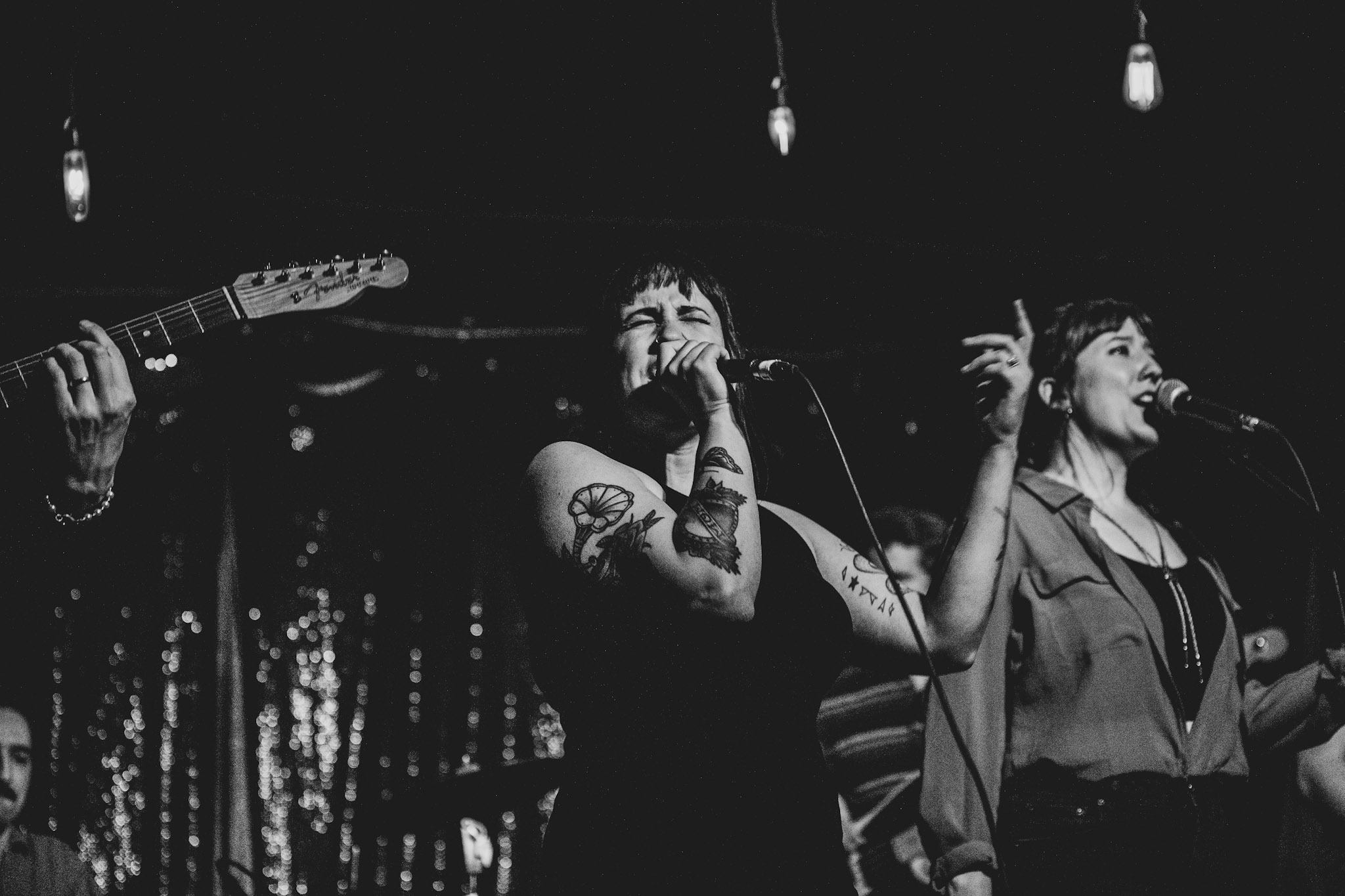 A woman, wearing a sleeveless top, grips a microphone with her right hand as she sings into it on stage.