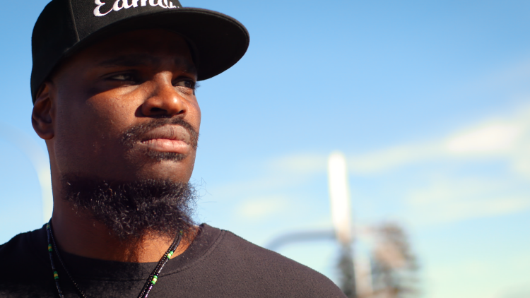 Close-up of Andrew Parker, a Black man, looking off to the right. He’s wearing a black shirt and black cap with the word ‘Edmonton' stitched in white.