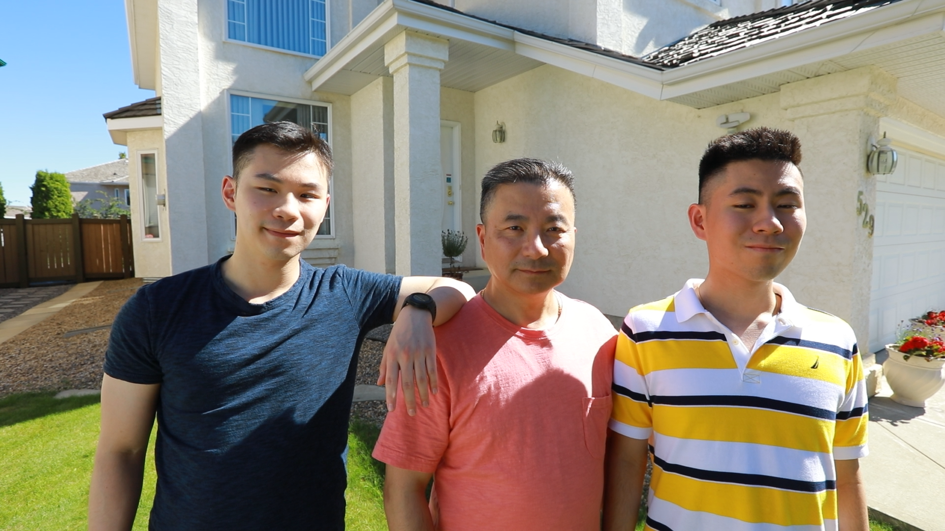 Three men, a father in between his two sons, stand outside in front of a house.